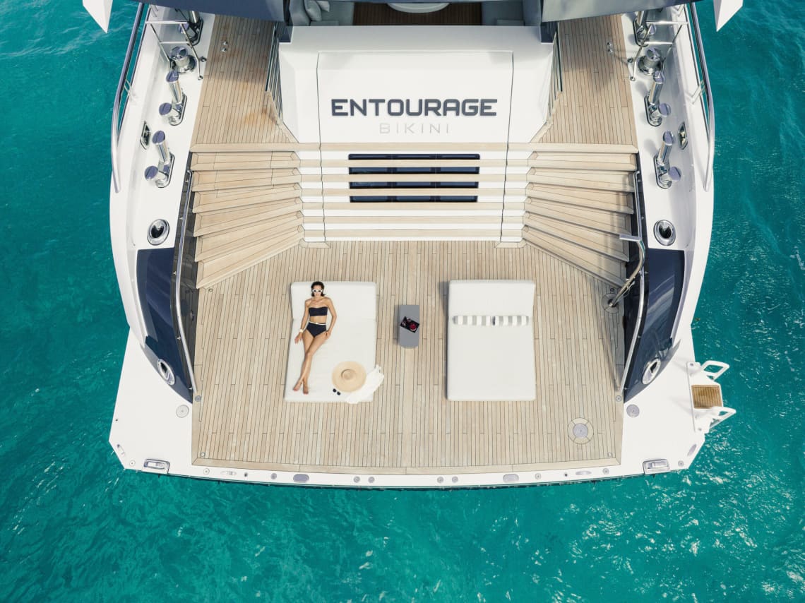 Woman in a black bikini lounging on a white couch at the back of a yacht