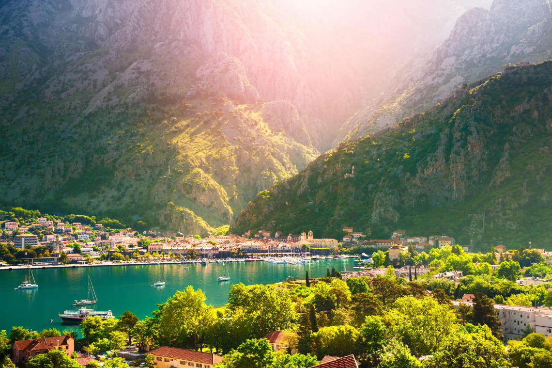 Sea in Montenegro with a town boardering it and huge mountains in the background