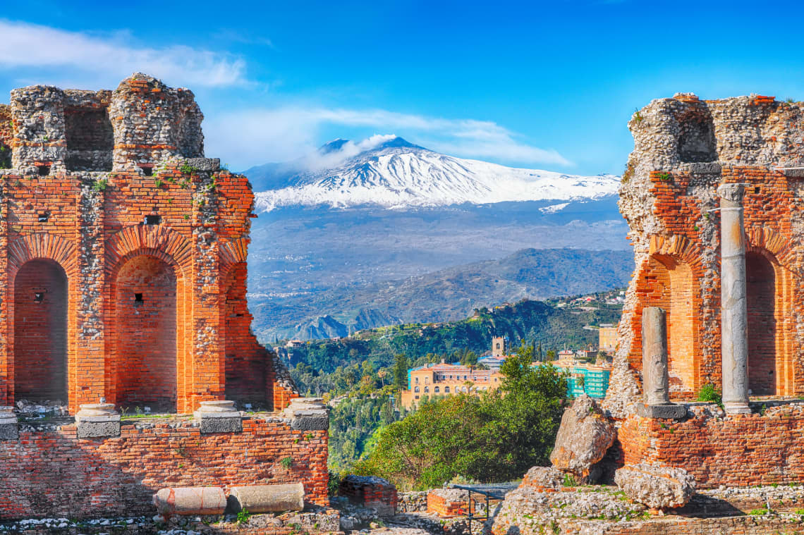 Ruins of ancient Greek theater in Taormina and Etna volcano in the background