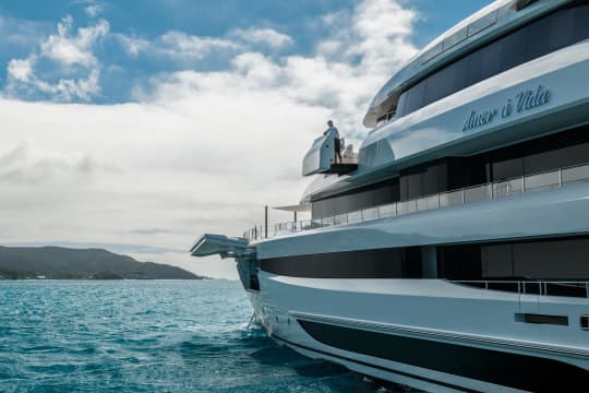 The side of a yacht on teal waters with an inspector on the boat