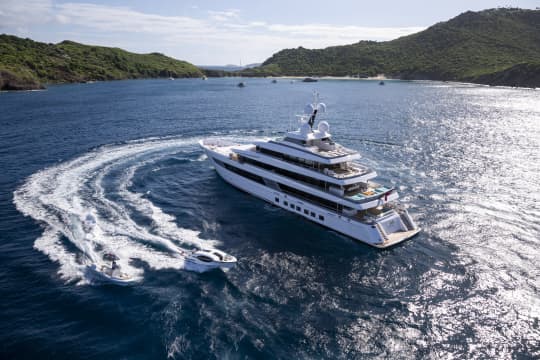 Yacht inbetween green mountains with 2 smaller boats