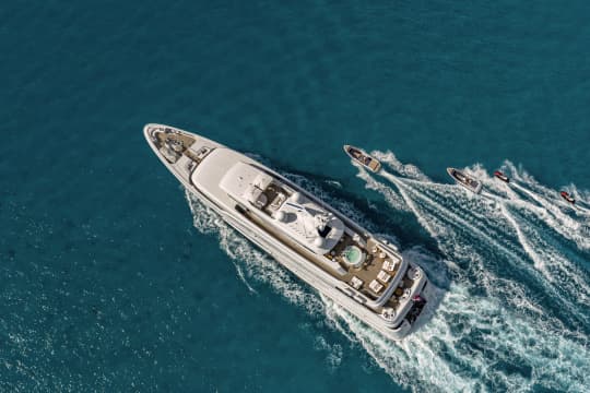 Yacht, 2 smaller boats, and 2 jetskis riding in clear teal water