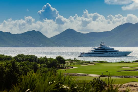Yacht Sailing on blue waters, with green grass in the foreground and beautiful mountains in the background