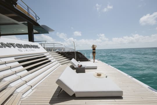 Woman walking along the edge of a yacht in a black bikini where sleek couches are