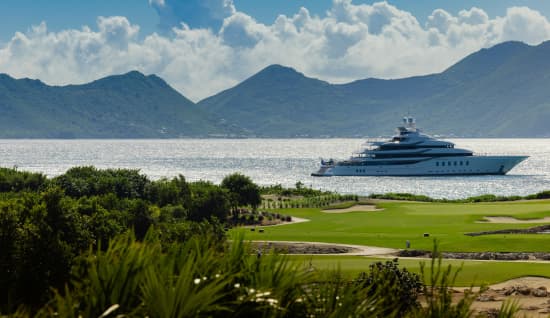 Yacht Sailing on blue waters, with green grass in the foreground and beautiful mountains in the background